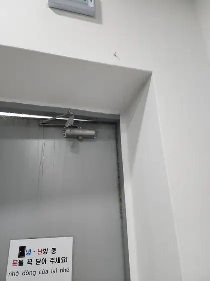 출입문 힌지 — 도어클로저가 달린 회색 철문